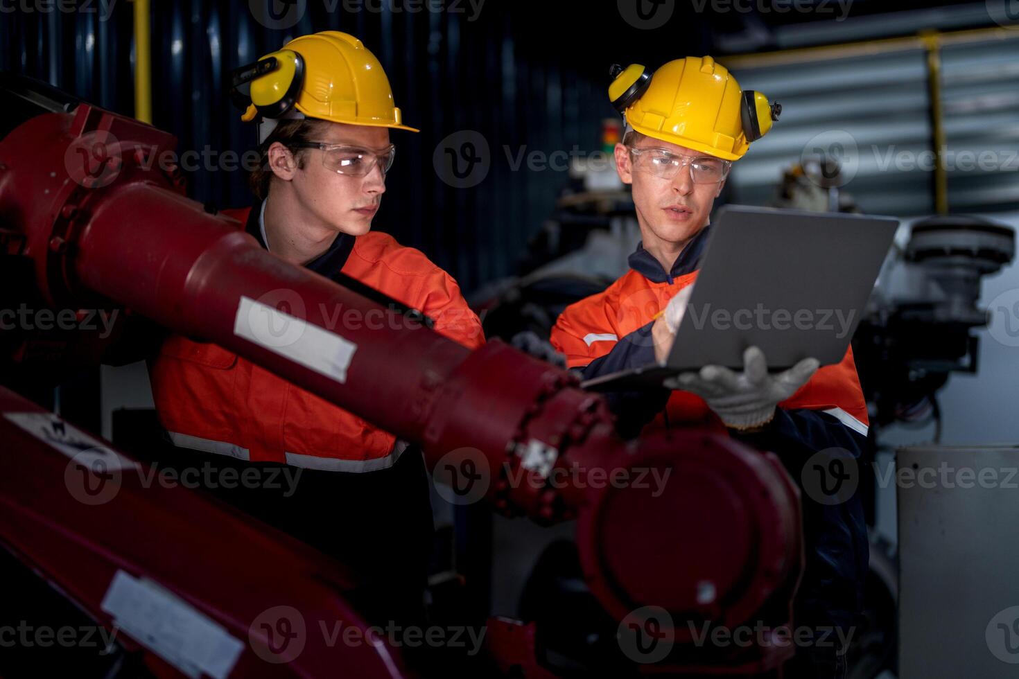 group of male engineer workers maintenance automatic robotic arm machine in a dark room factory. worker checking and repairing automatic robot hand machine. Worker wearing safety glasses and helmet. photo