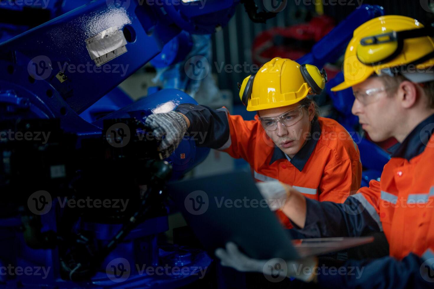 Factory engineers inspecting on machine with smart tablet. Worker works at heavy machine robot arm. The welding machine with a remote system in an industrial factory. Artificial intelligence concept. photo