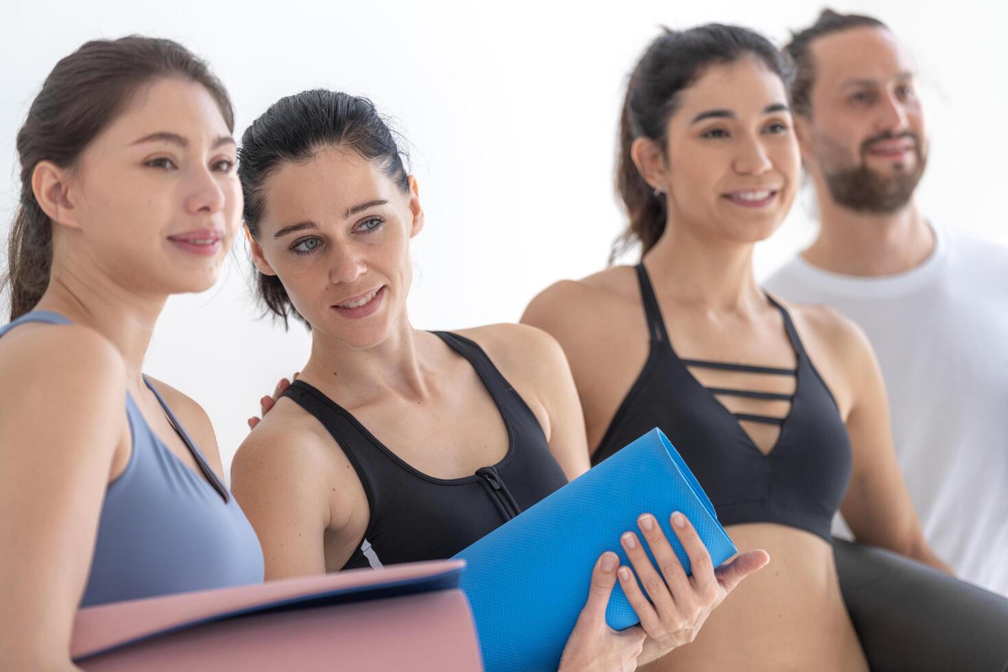 Group of happy sporty women and guy wearing body stylish sportswear holding personal carpets leaned on a white background. waiting for yoga class or body weight class. healthy lifestyle and wellness photo