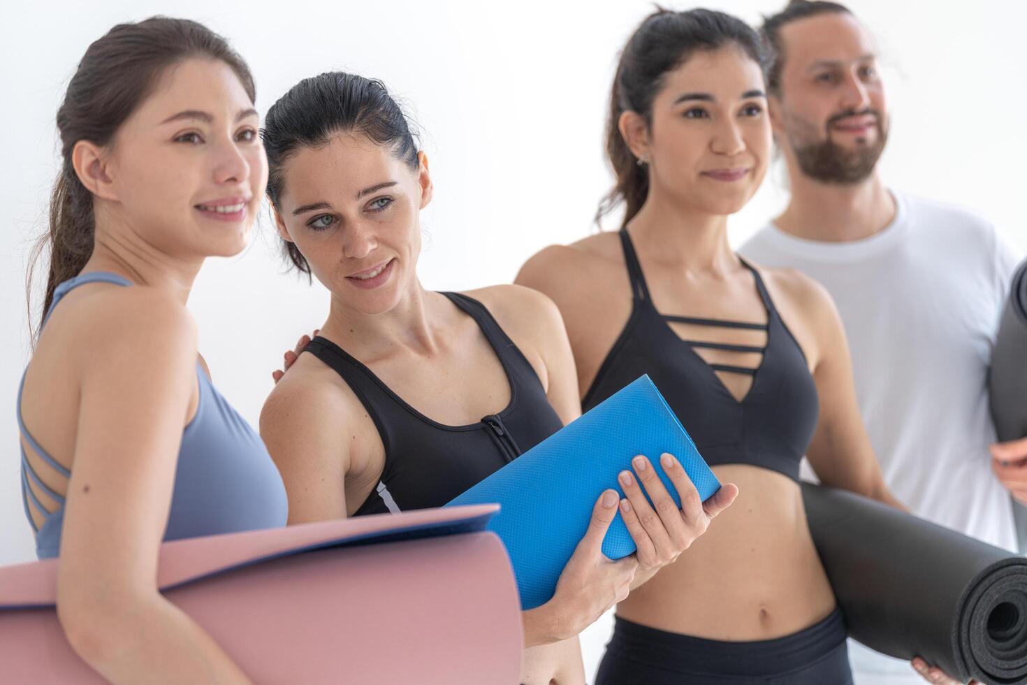 Group of happy sporty women and guy wearing body stylish sportswear holding personal carpets leaned on a white background. waiting for yoga class or body weight class. healthy lifestyle and wellness photo