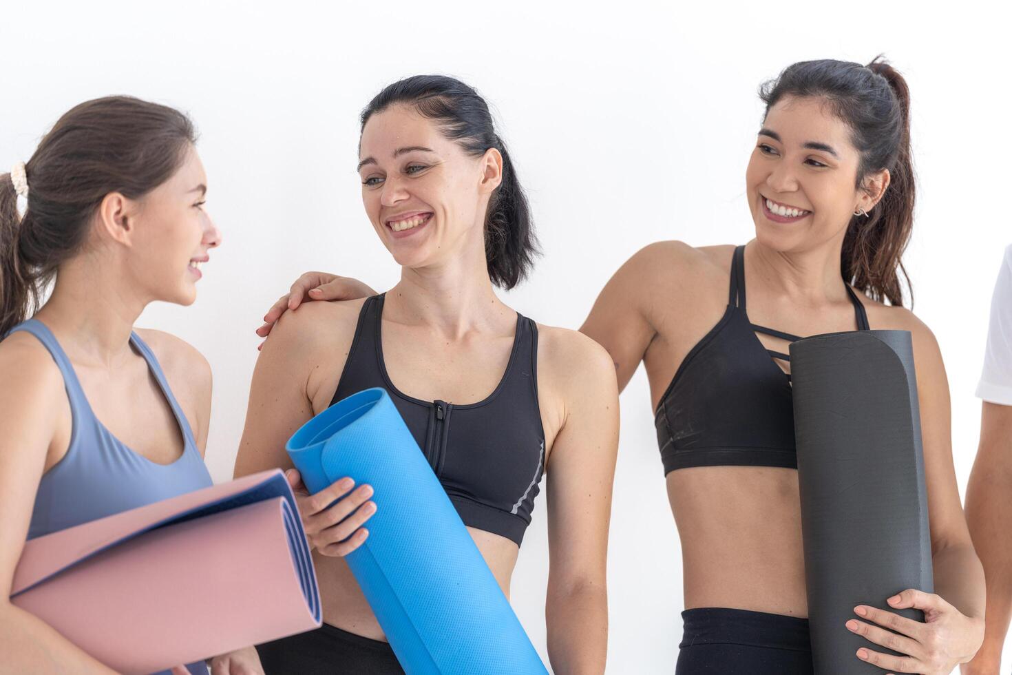 grupo de contento deportivo mujer hablando con cuerpo elegante ropa de deporte participación personal alfombras inclinado en un blanco antecedentes. esperando para yoga clase o cuerpo peso clase. sano estilo de vida y bienestar foto