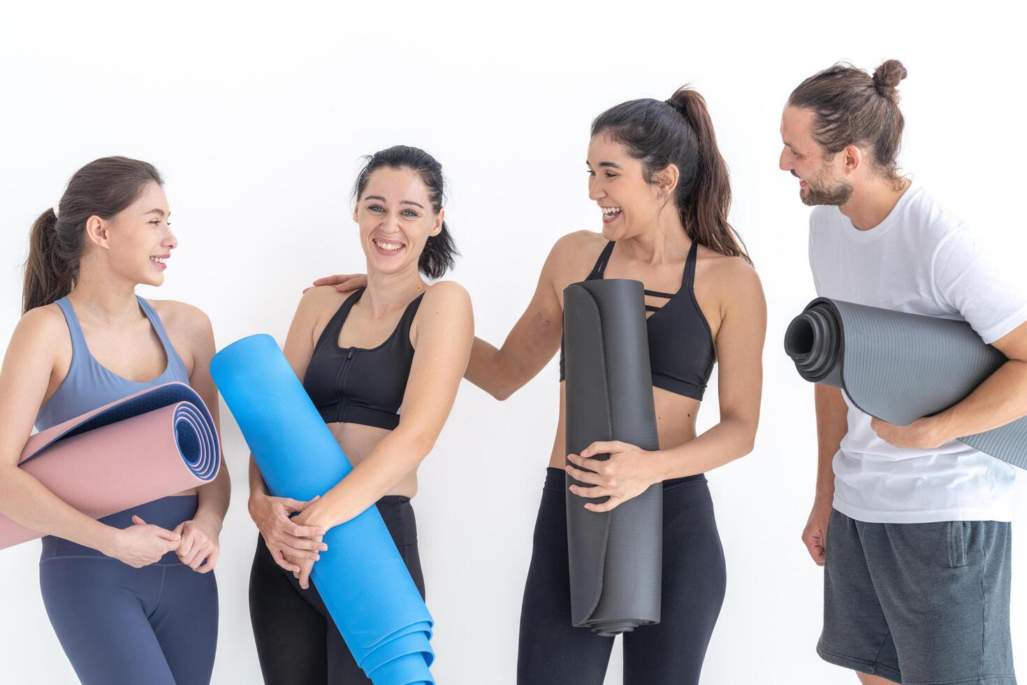 Group of happy sporty women talking with body stylish sportswear holding personal carpets leaned on a white background. waiting for yoga class or body weight class. healthy lifestyle and wellness photo