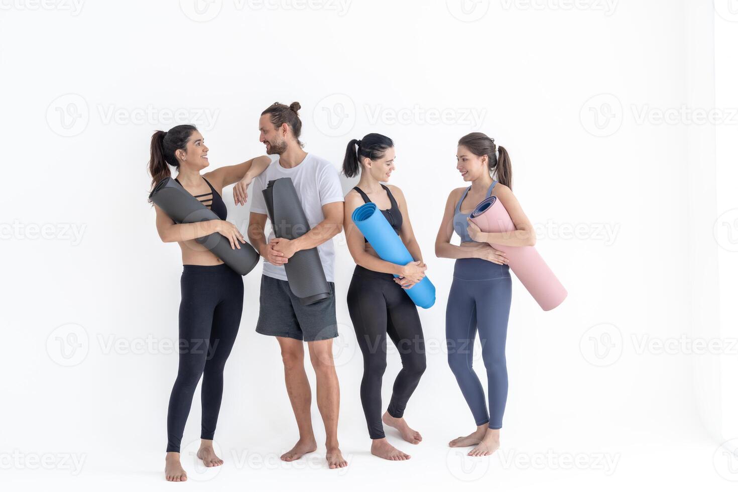 grupo de contento deportivo muchachas y chico vistiendo cuerpo elegante ropa de deporte participación personal alfombras inclinado en un blanco antecedentes. esperando para yoga clase o cuerpo peso clase. sano estilo de vida y bienestar foto