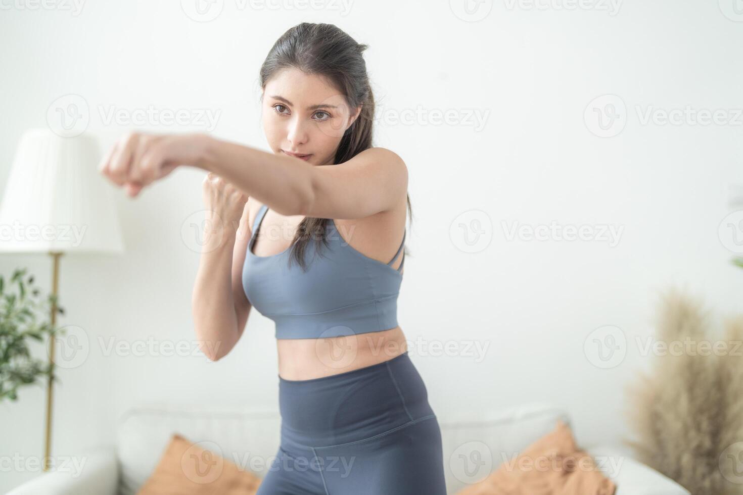 atractivo y fuerte mujer extensión antes de aptitud a interior casa. sano estilo de vida. mujer calentar arriba por boxeo en el aire. joven hembra con Delgado cuerpo puñetazos boxeo juego de piernas cardio ejercicio. foto