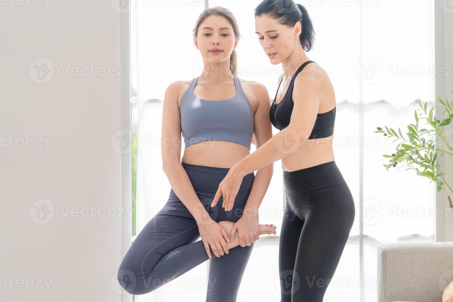 Two women confident training yoga. Athletic women in sportswear doing fitness stretching exercises at home in the living room. Sport and recreation concept. Yoga teacher is helping young woman. photo
