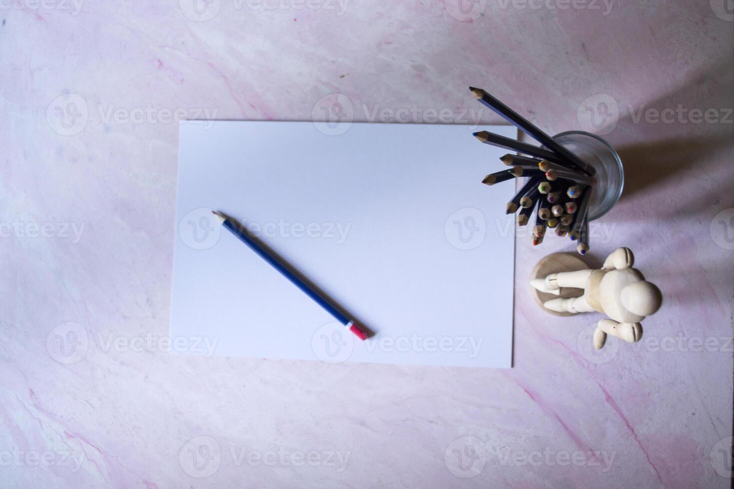 Colored pencils, empty paper and dummy for drawing on the table. photo