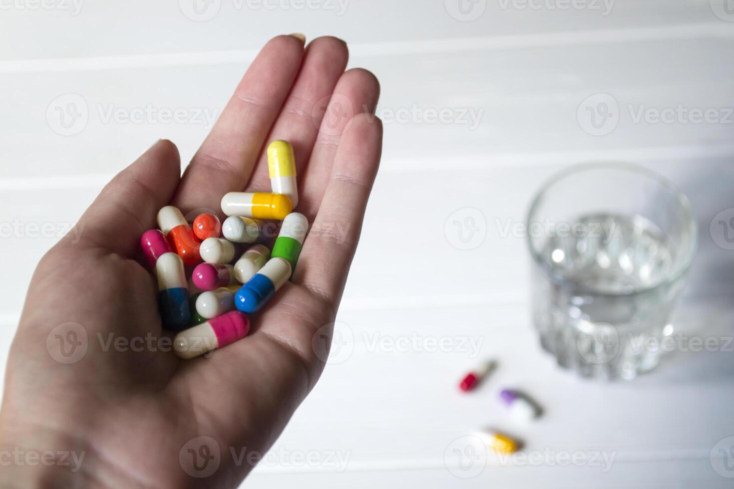A capsules in hand and a glass of water against a white background. photo