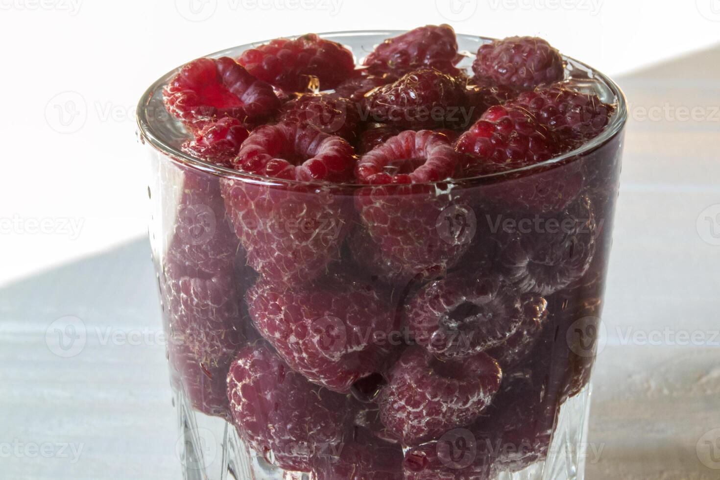 Ripe raspberries in a glass with water, on a white wooden background. photo