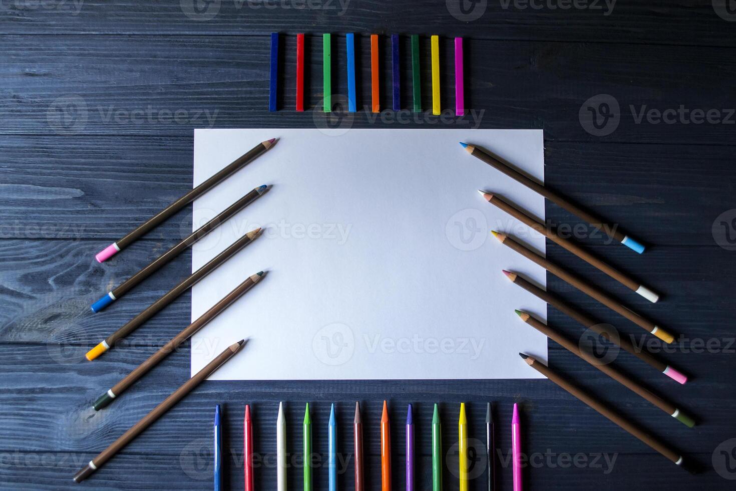 Palette of multicolored pencils and the sheet of white paper on dark blue wooden desk. photo