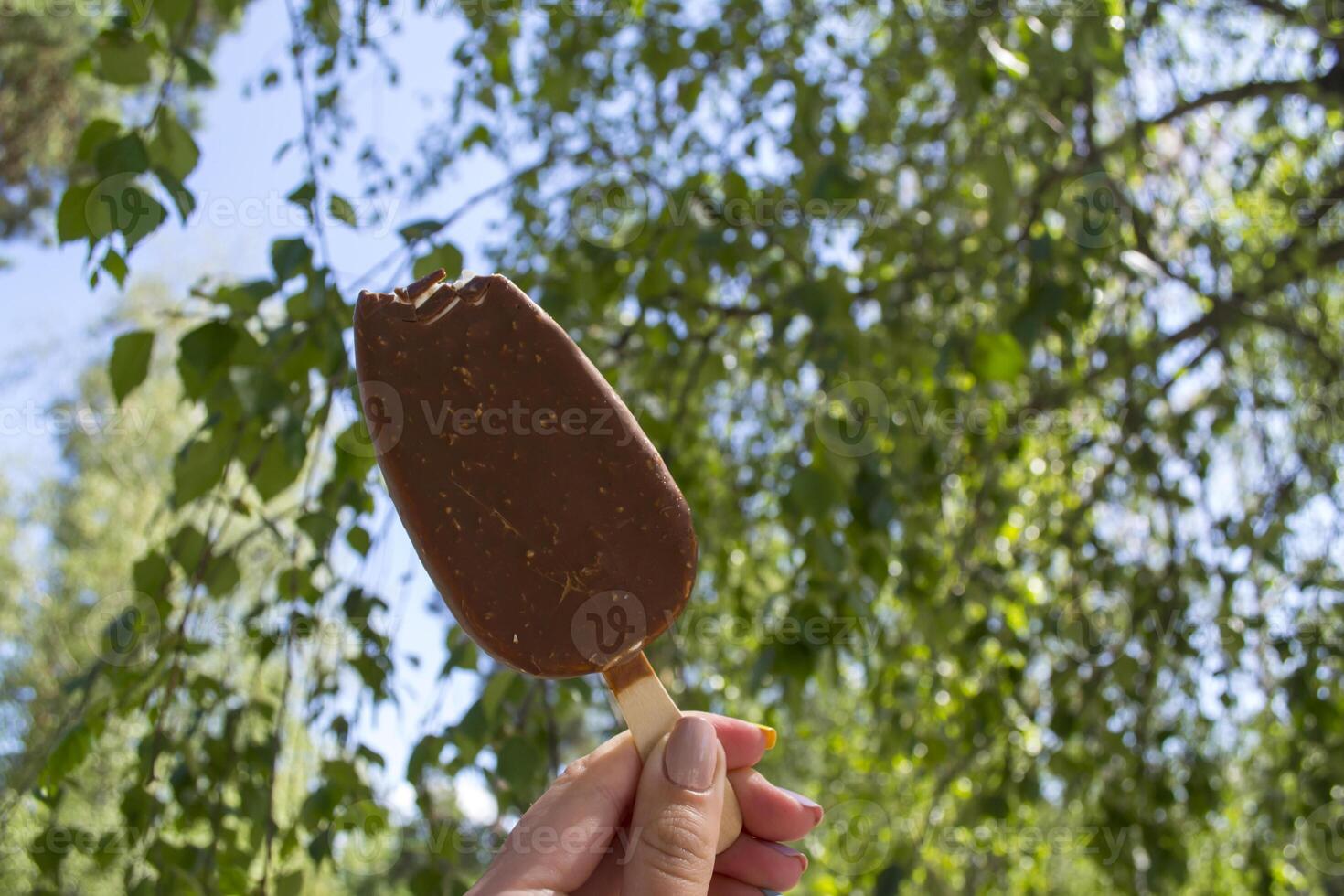 An ice cream in female arm against a green tree background. photo
