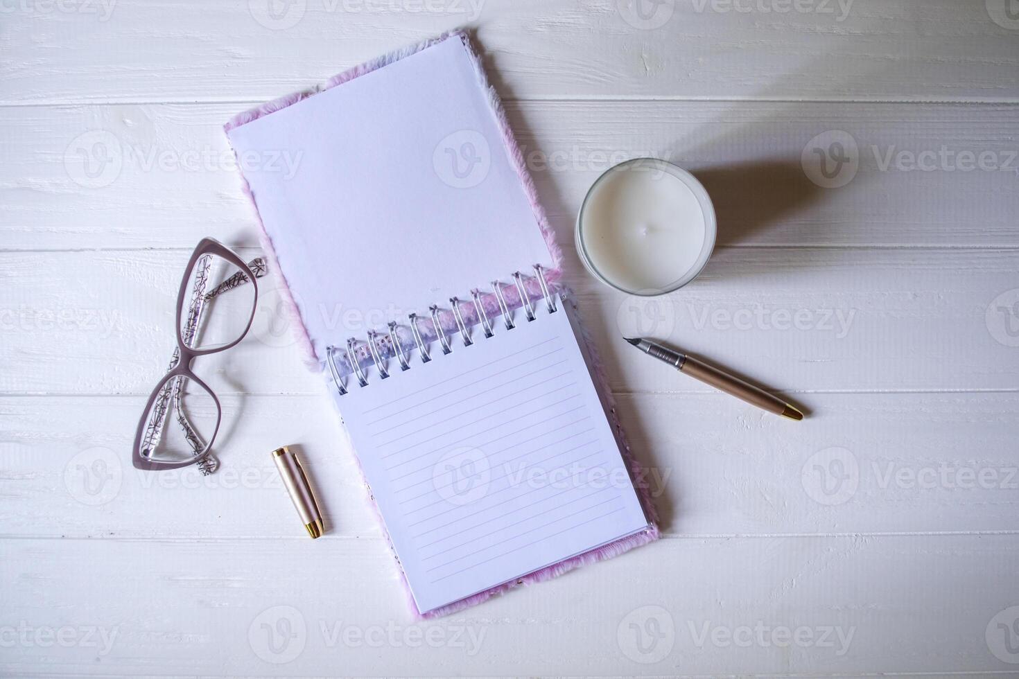 The opened notepad, pen, white candle, glasses and branches of hops as decoration on a white wooden table. Desktop still life with space for text. photo
