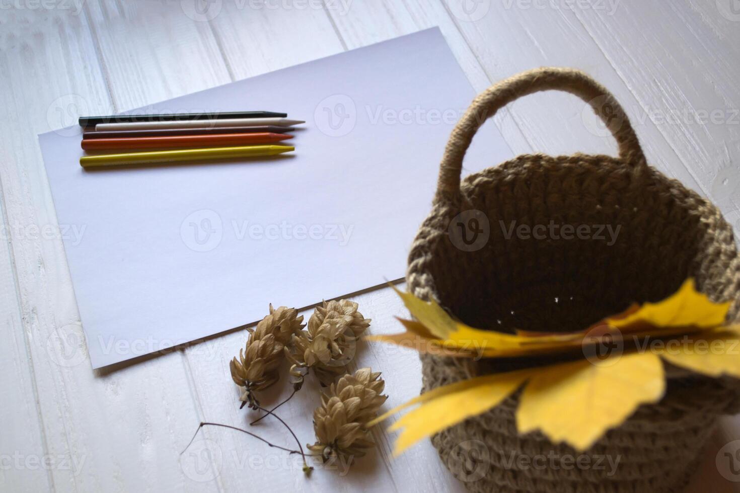 White paper, multi-color pencils and autumn leaves in a basket on the desk. photo