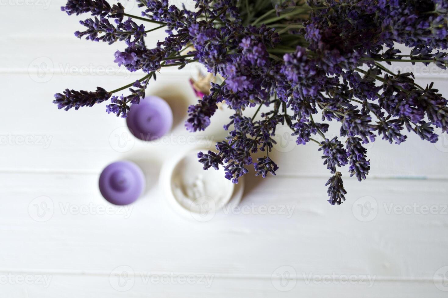 Lavender flowers, candles and cream on a white wooden background. Beauty care. Top view. photo