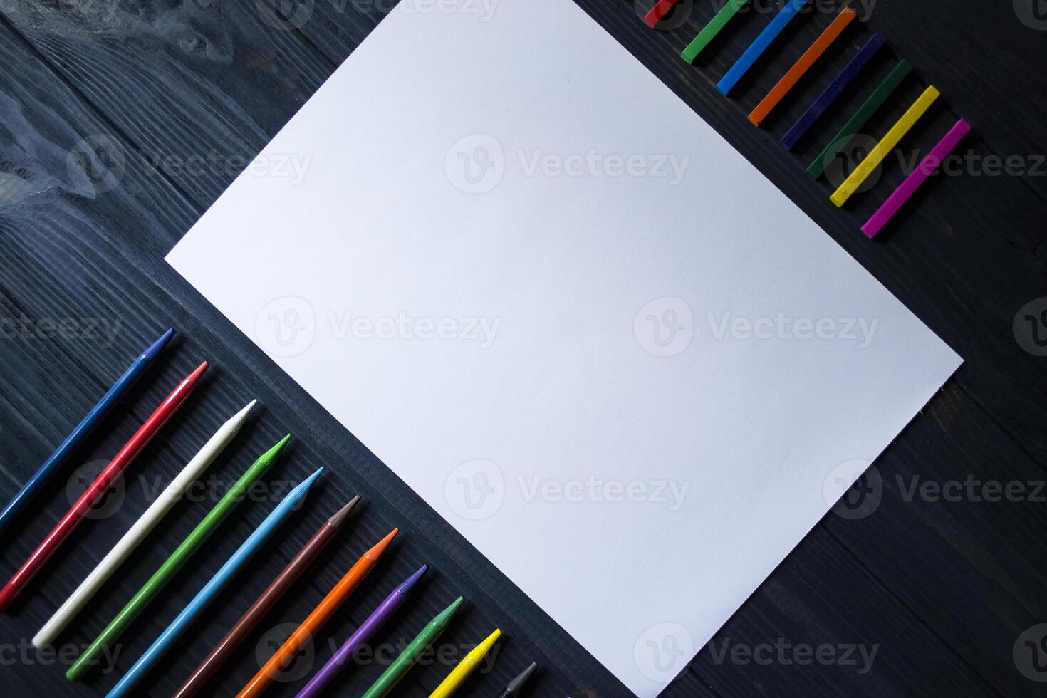 Palette of multicolored pencils and the sheet of white paper on dark blue wooden desk. photo