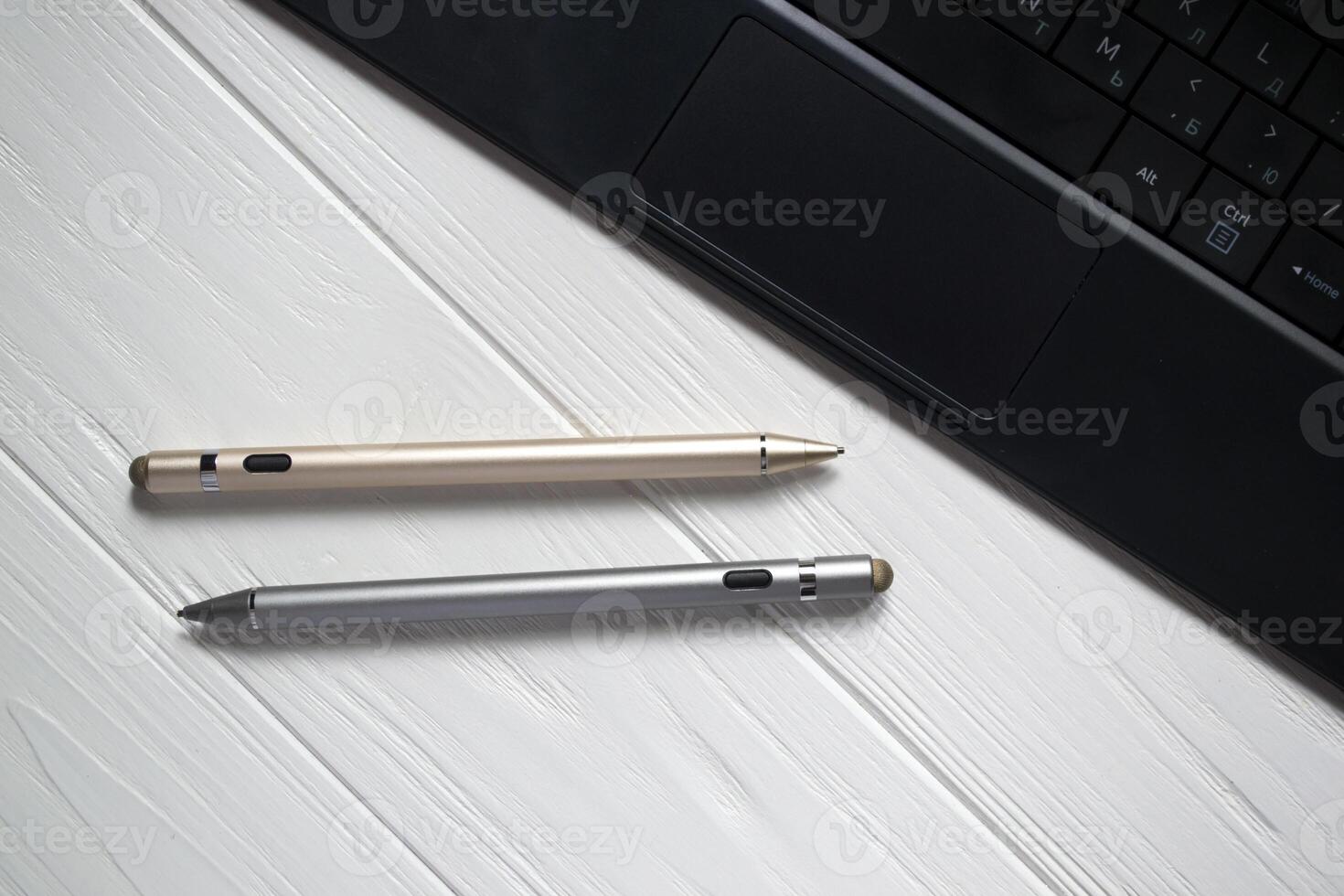 Gold and silver stylus pens with keyboard on a white wooden background close up. photo