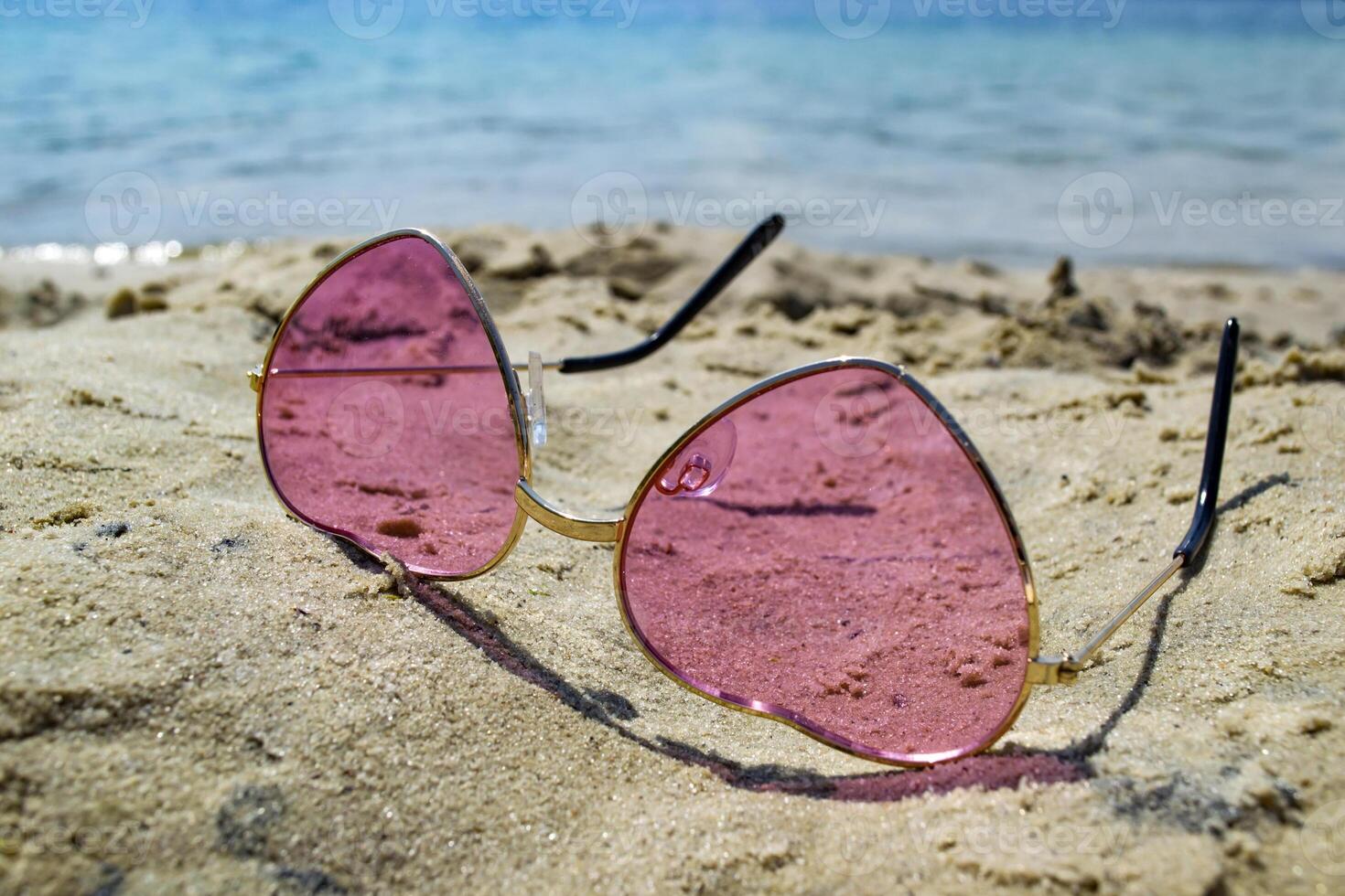 Pink glasses on the sand near blue water of lake. photo