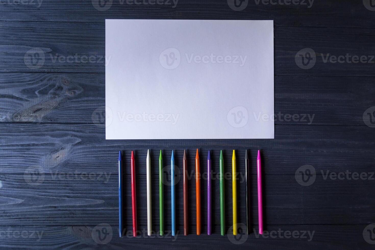 Palette of multicolored pencils and the sheet of white paper on dark blue wooden desk. photo