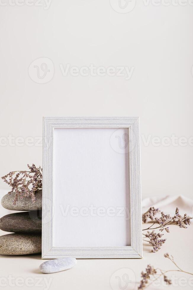 An empty photo frame near a stack of stones and dried flowers on a light background vertical view