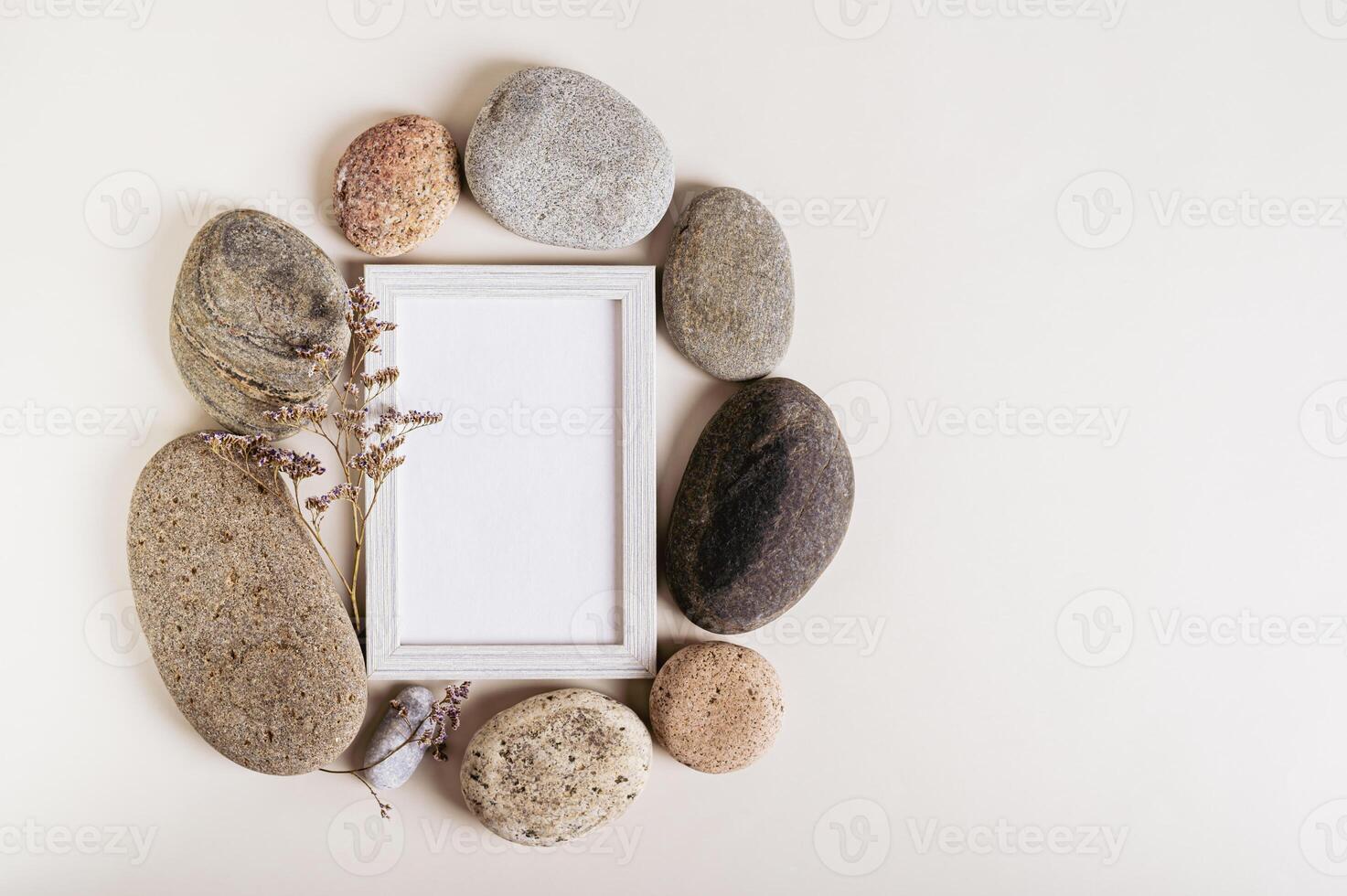 Empty photo frame with a dry flower surrounded by stones on a light background
