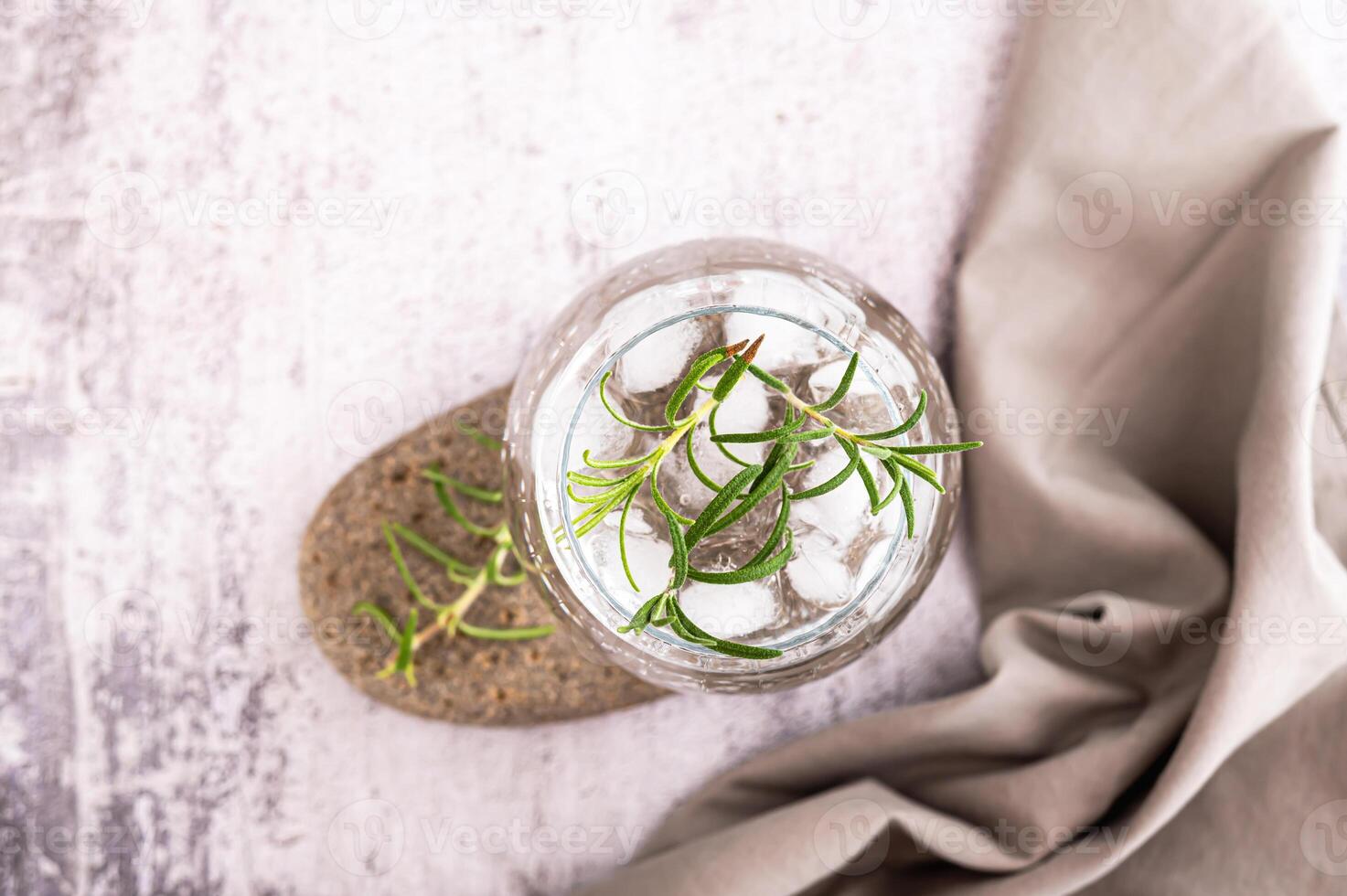 Close up of gin tonic with ice and rosemary in a glass on a stone on the table top view photo