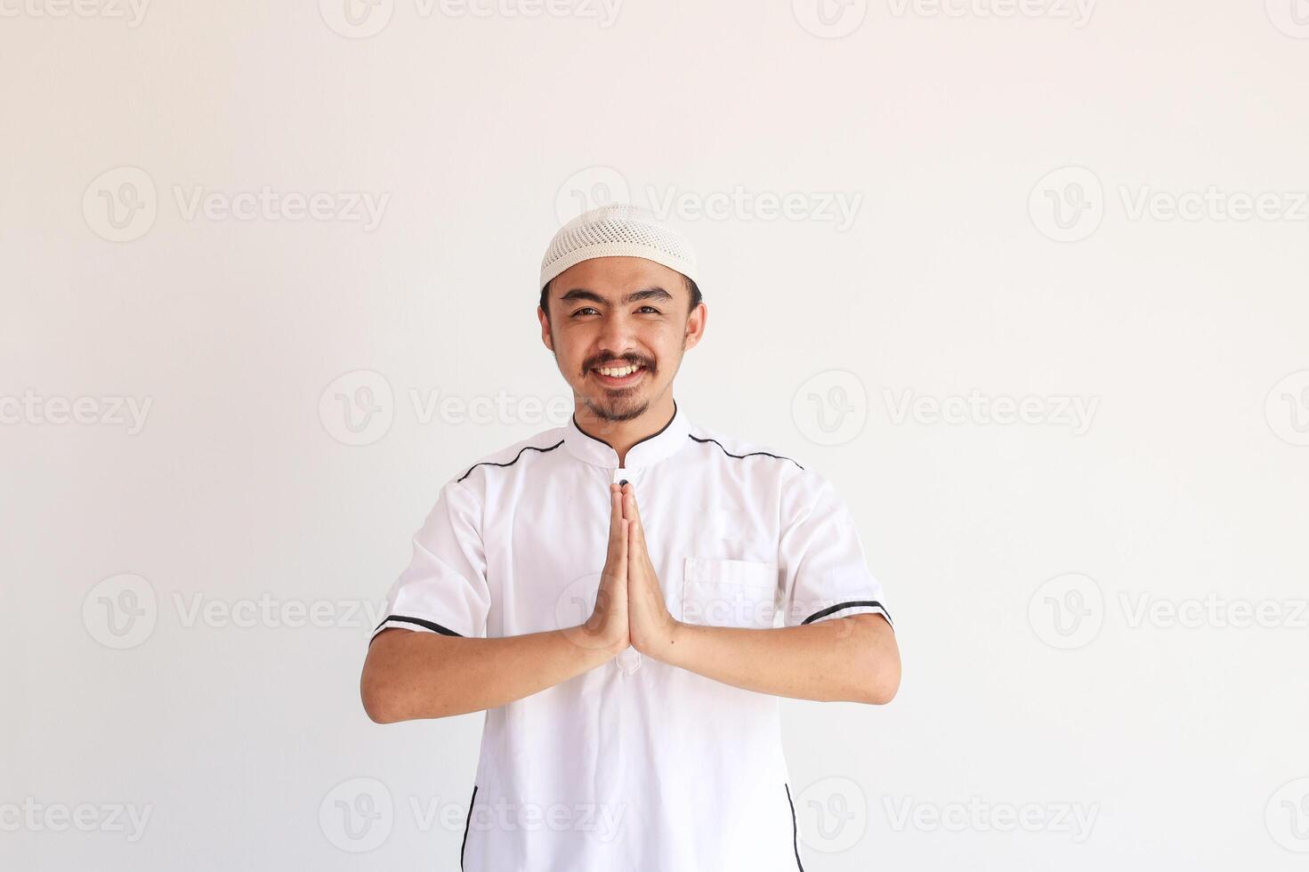 Smiling Young Asian Muslim Man in Baju Koko Standing with Gesturing Eid Mubarak Greeting photo