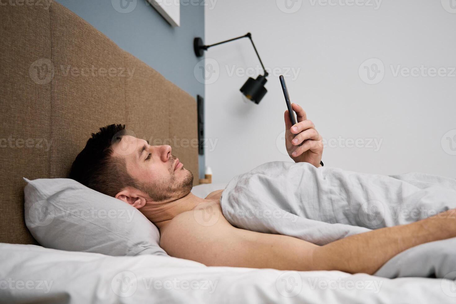 Phone addiction. Man lying in bed with smartphone photo