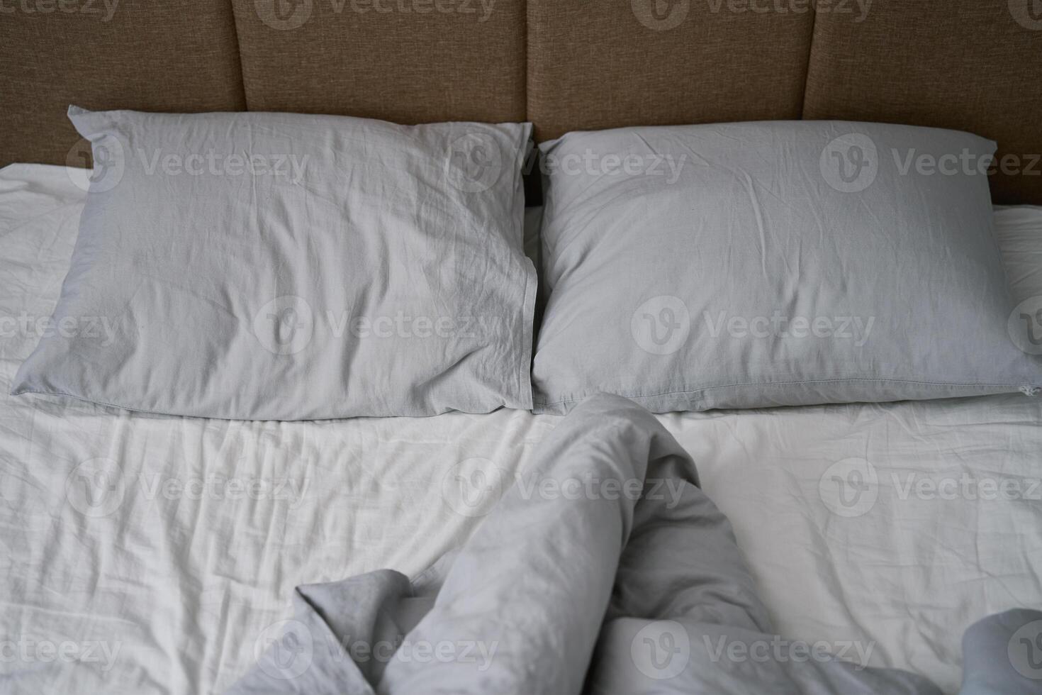 Crumpled bed with pillows, blanket and crumpled sheets in bedroom photo