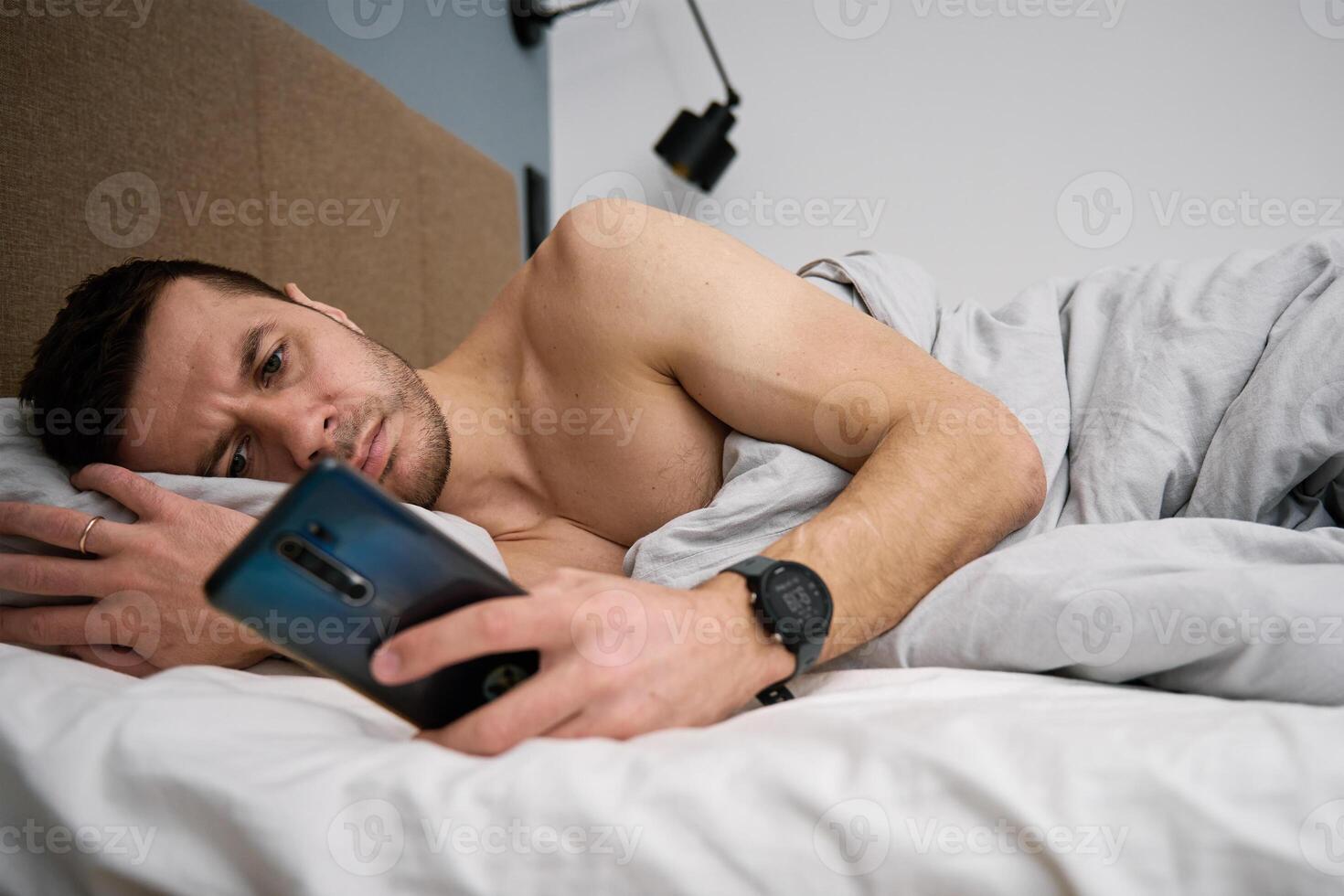 Phone addiction. Man lying in bed with smartphone photo