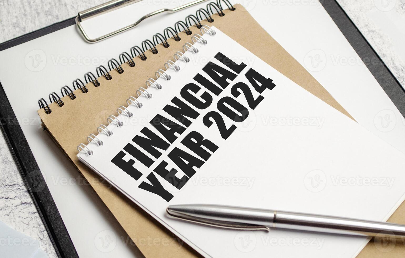 Notebook with FINANCIAL YEAR 2024 inscription on clipboard. Office financial planning concept with pen on vintage background photo