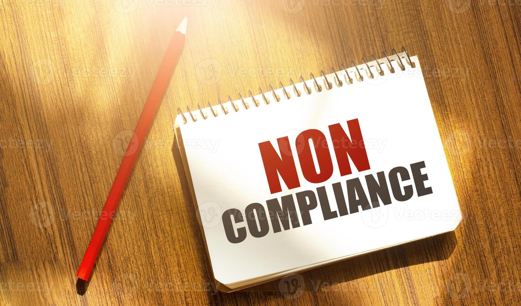 NON COMPLIANCE message on notepad with pencil on wooden background photo