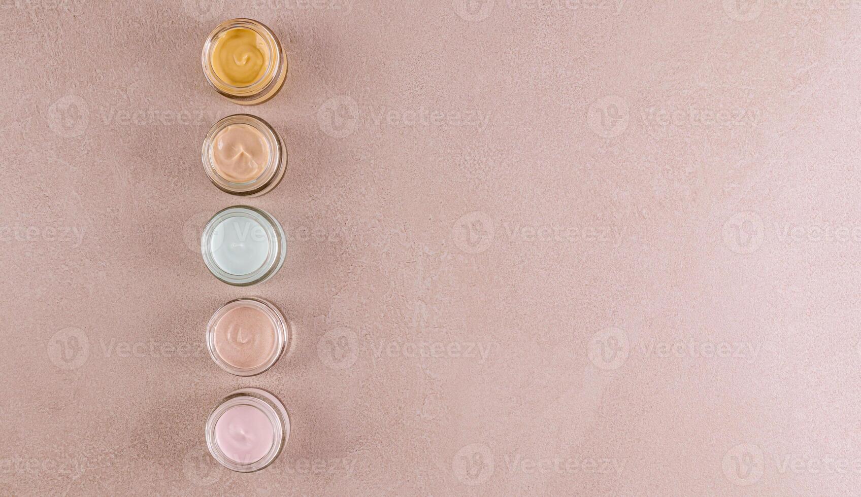 A vertical row of jars with cosmetic cream of different textures and colors for face and body skin care. Beige background. space for text. Top view. photo