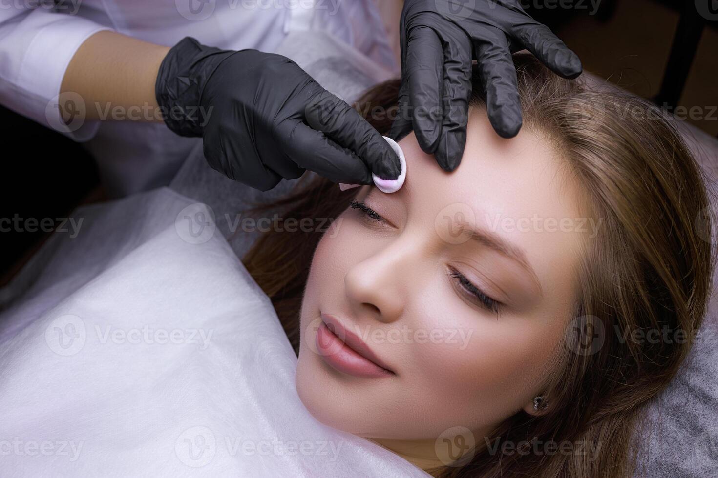 Close-up of degreasing the surface of the eyebrows with a cotton sponge. PMU Procedure, Permanent Eyebrow Makeup. photo