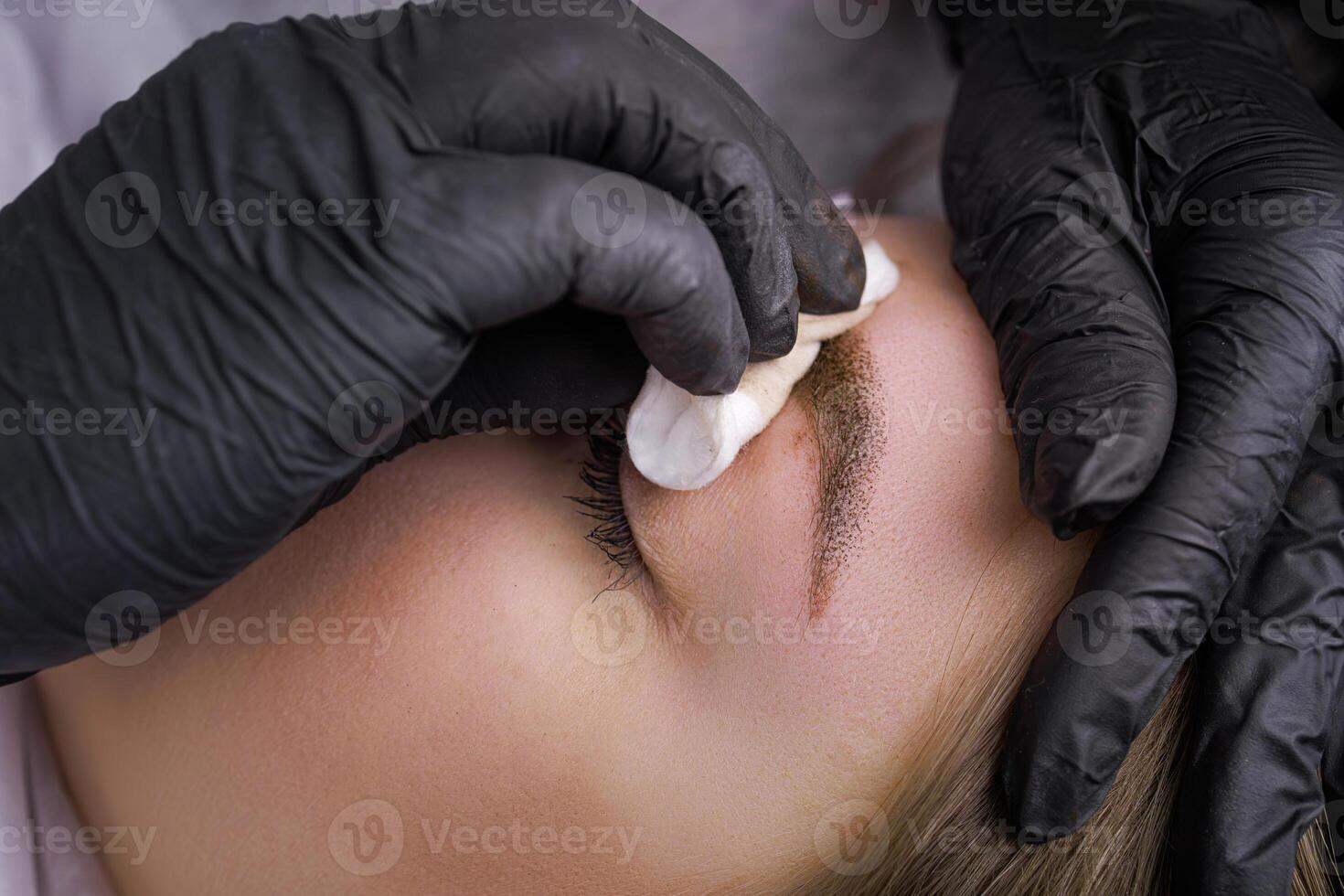 Remove excess pigment from the eyebrows with a cotton sponge. PMU Procedure, Permanent Eyebrow Makeup. photo