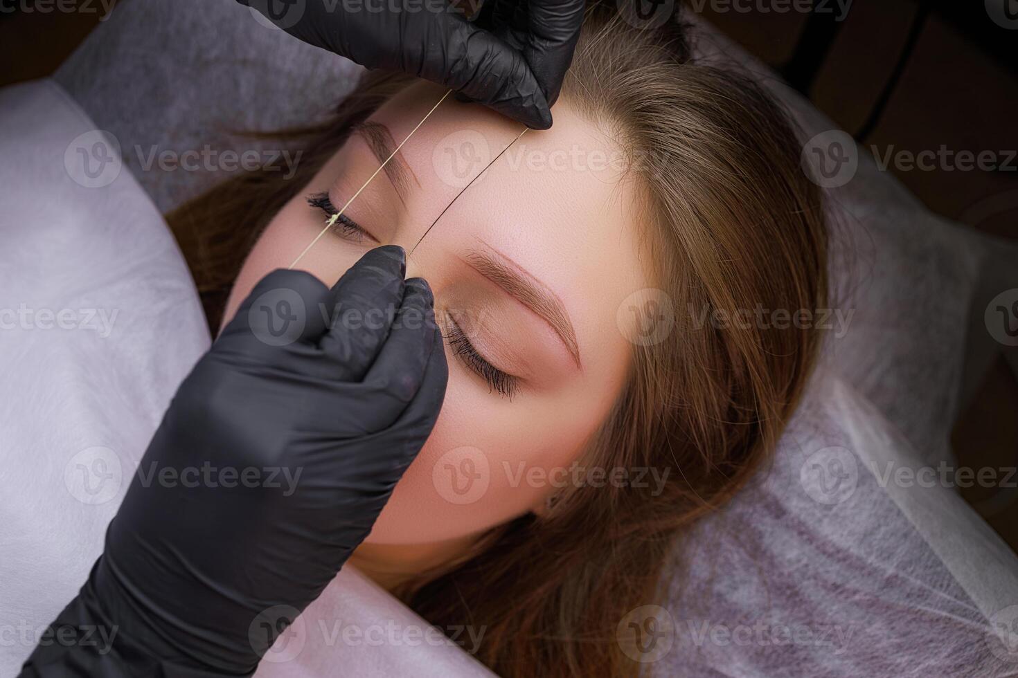 Before the permanent makeup procedure, the master makes a marking with a thread on the model's eyebrows. PMU Procedure, Permanent Eyebrow Makeup. photo
