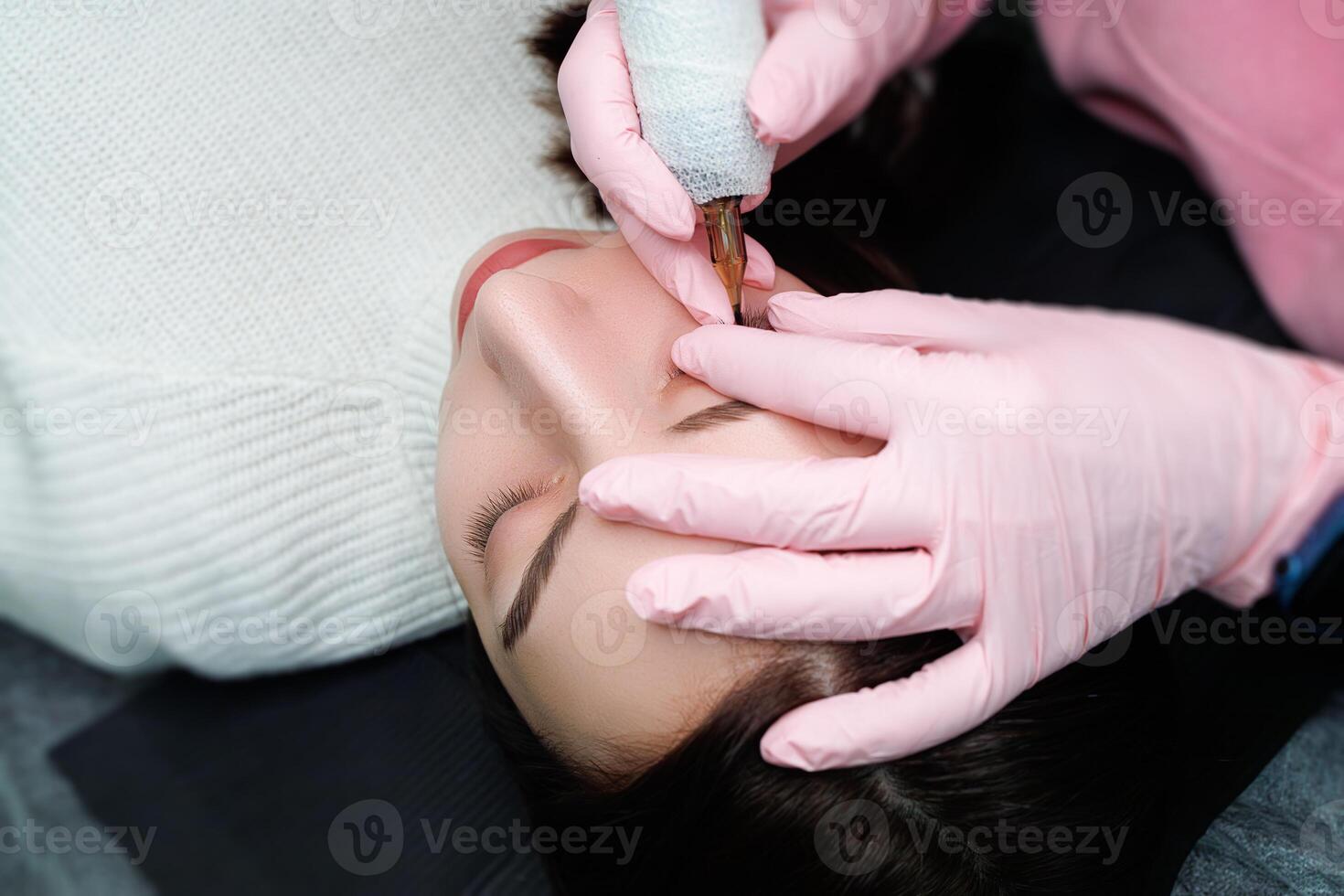 The master pulls the upper eyelid of the eye with his fingers to perform permanent makeup between the eyelashes. Permanent eye makeup and PMU eyelashes photo