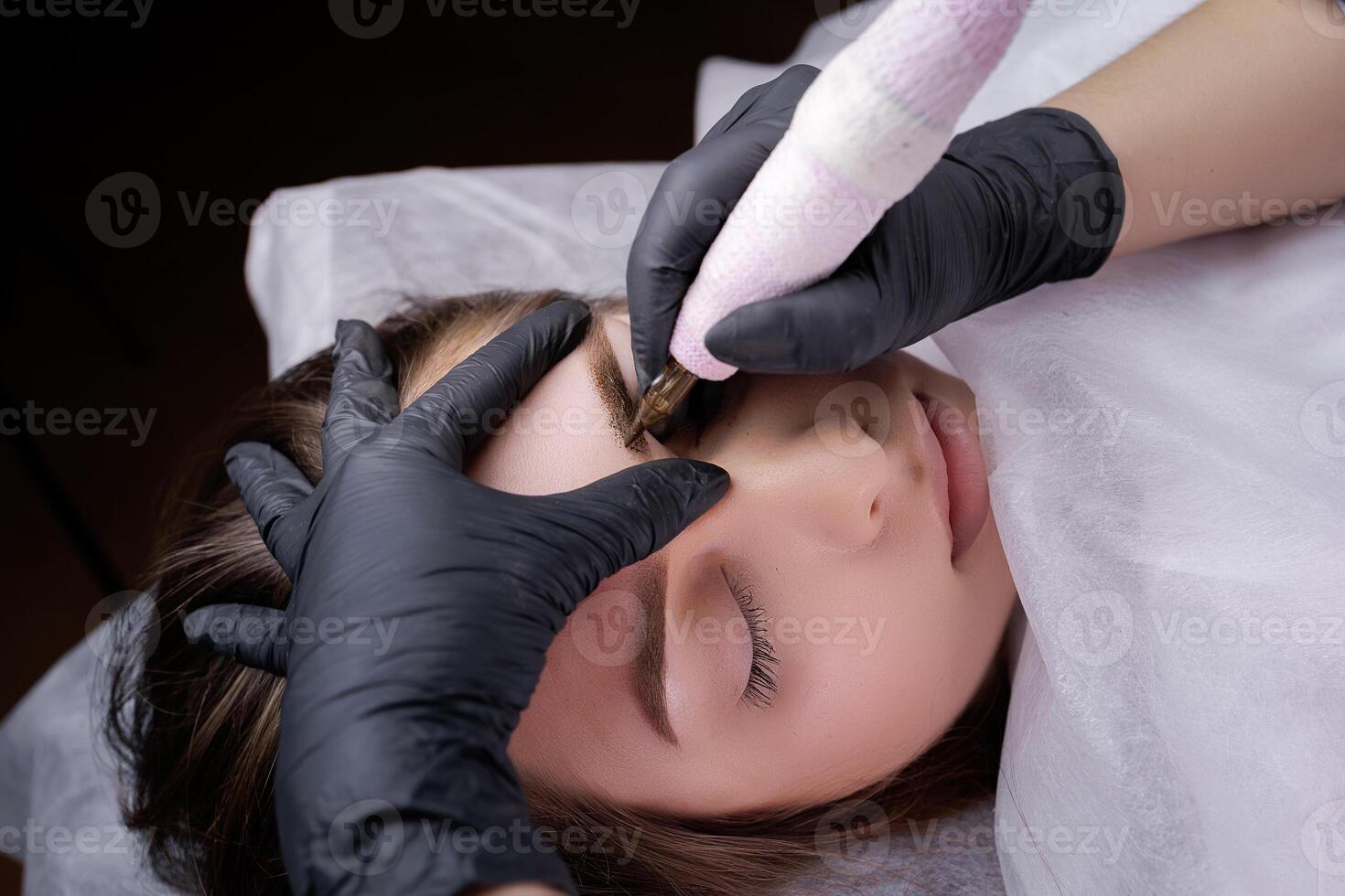 Completing permanent eyebrow makeup with a tattoo machine. PMU Procedure, Permanent Eyebrow Makeup. photo