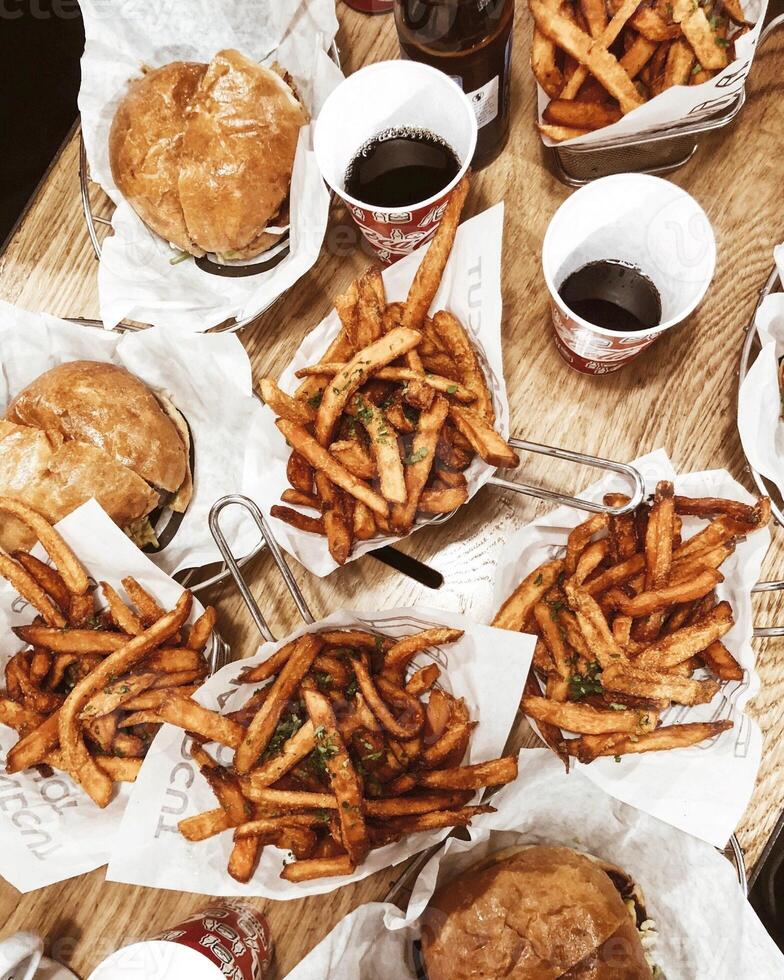 Top view of tasty french fries, hamburger and cola on wooden table photo