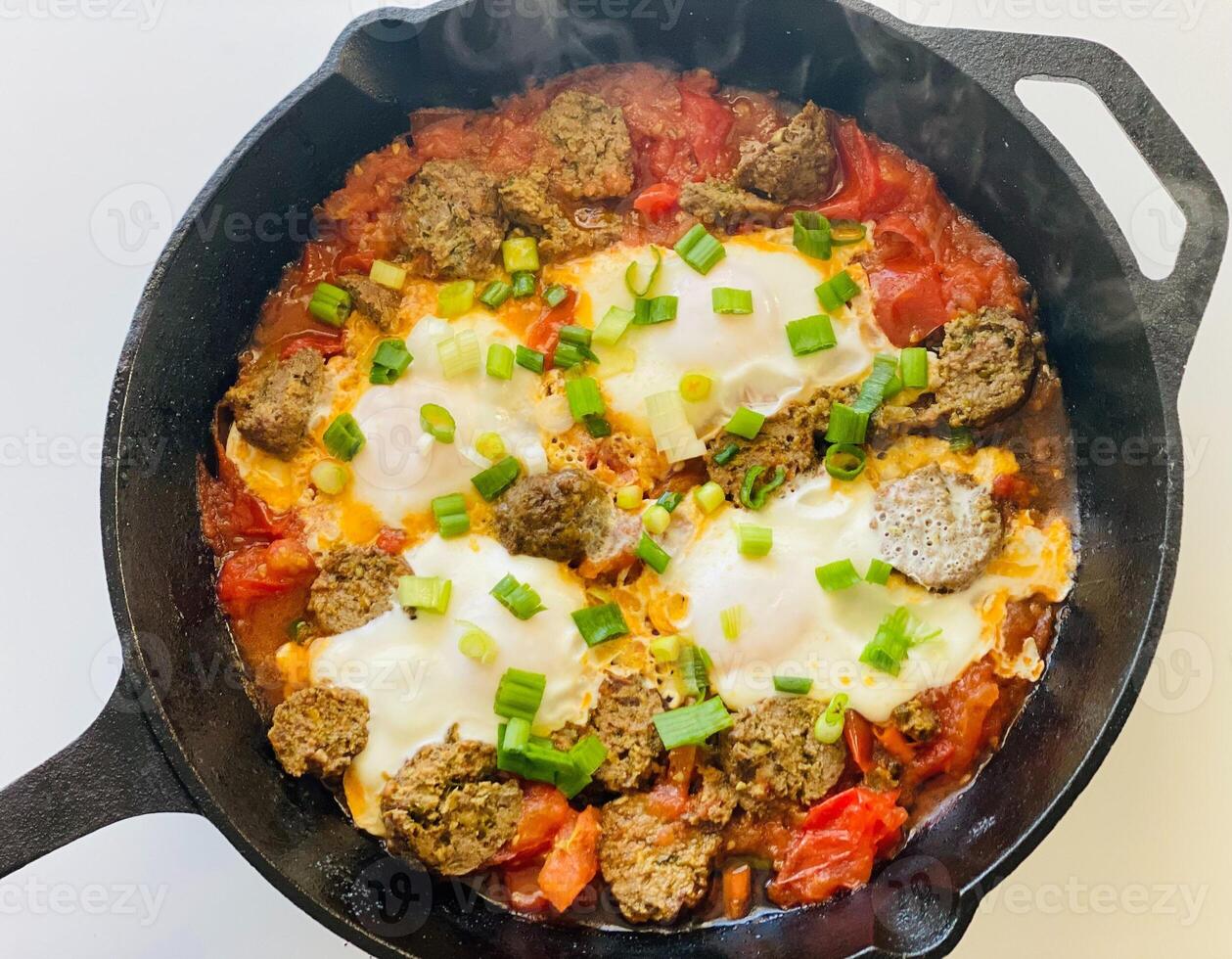 fried eggs with meat and vegetables in a cast-iron frying pan photo