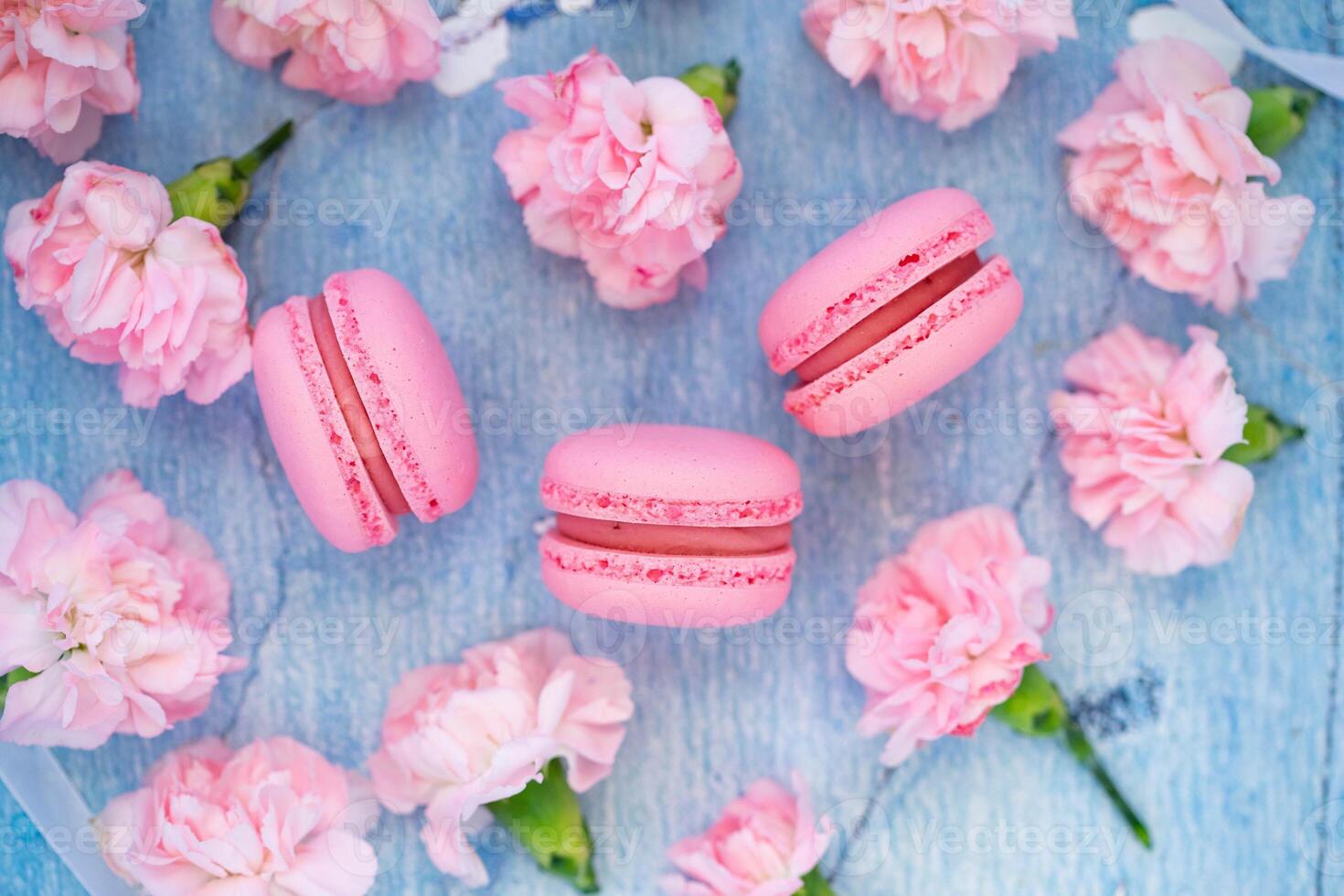 Pink macaroons on a blue wooden background with pink flowers. photo