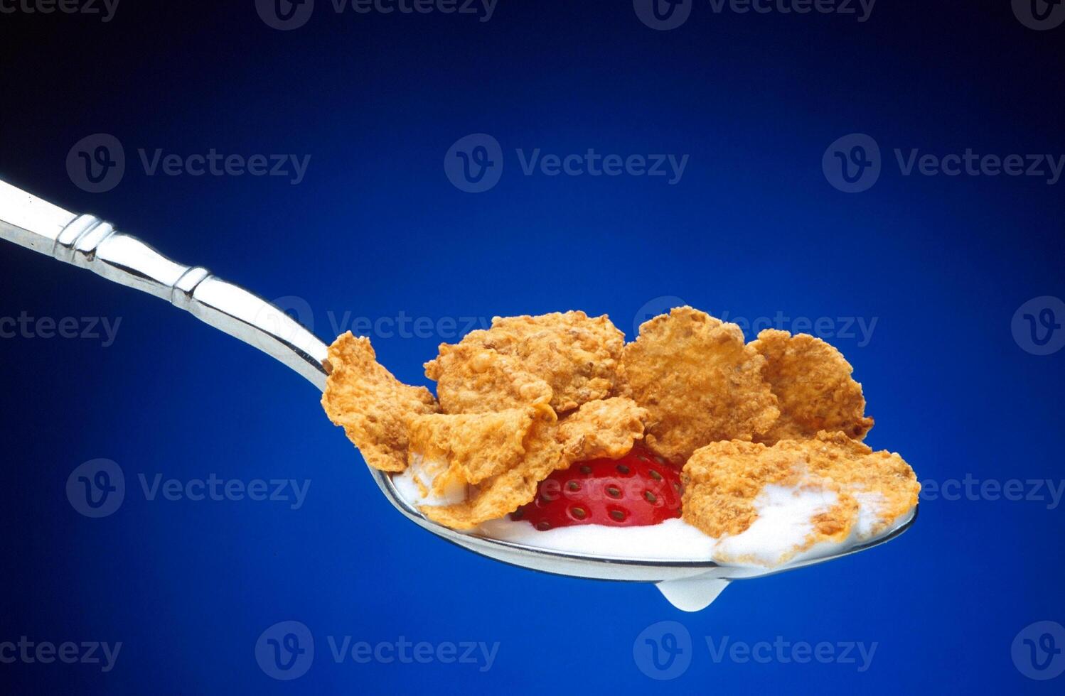 Spoonful of cornflakes with strawberry and yogurt on blue background photo