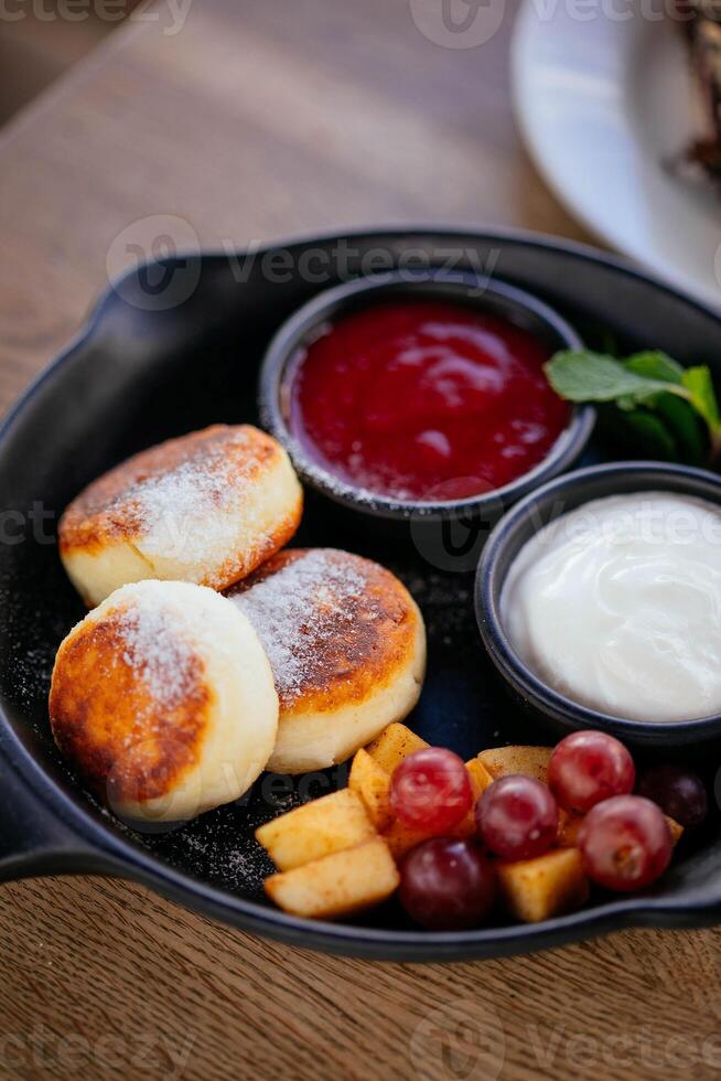 Cottage cheese pancakes with sour cream and fruit on a frying pan photo