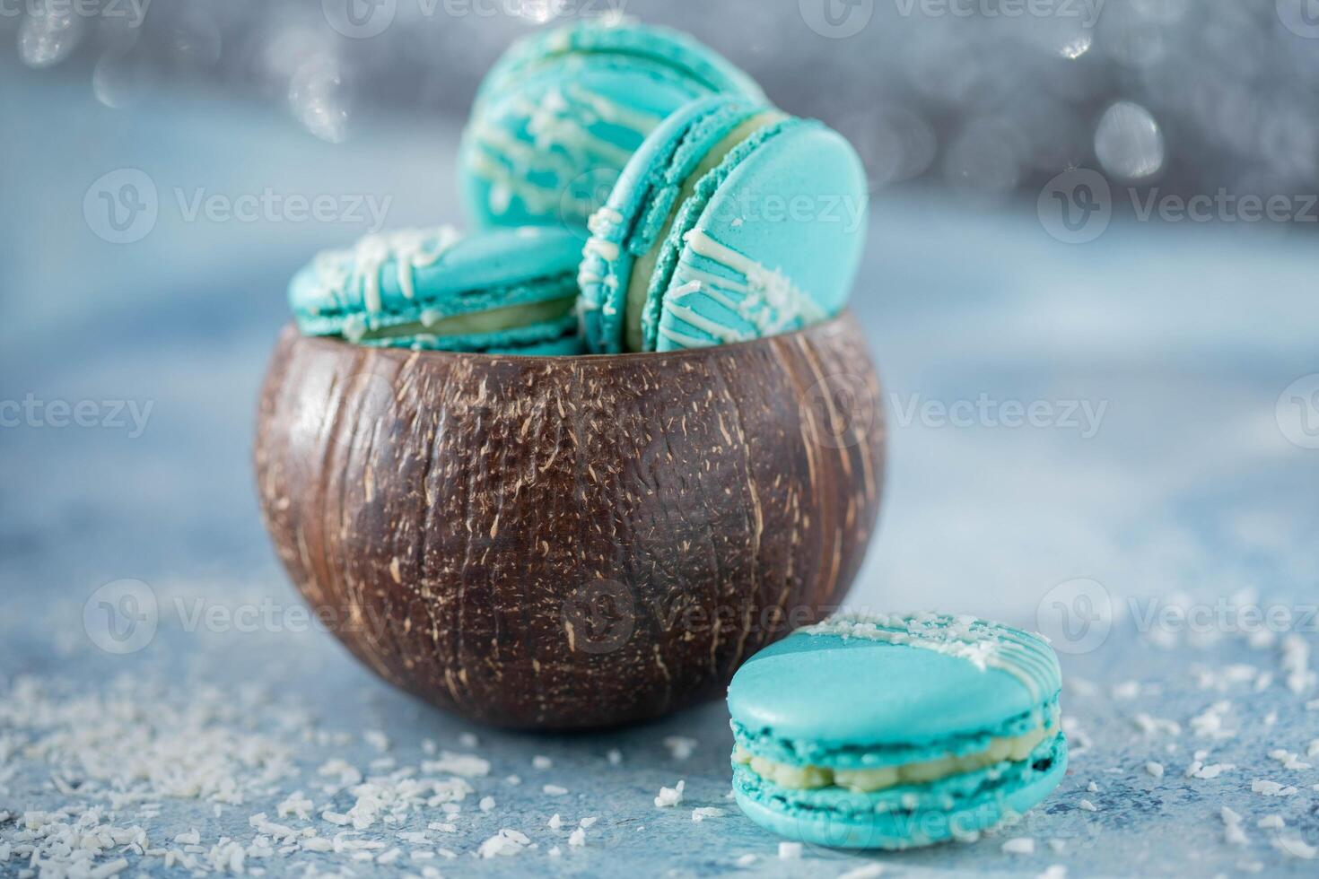 Tasty macaroons in coconut shell on blue background, closeup photo