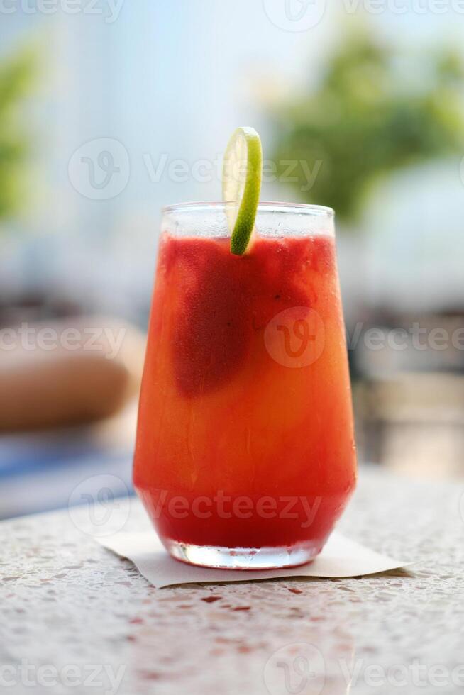 Close-up of a vibrant fruit mocktail adorned with a lime slice on a sunlit poolside table. photo