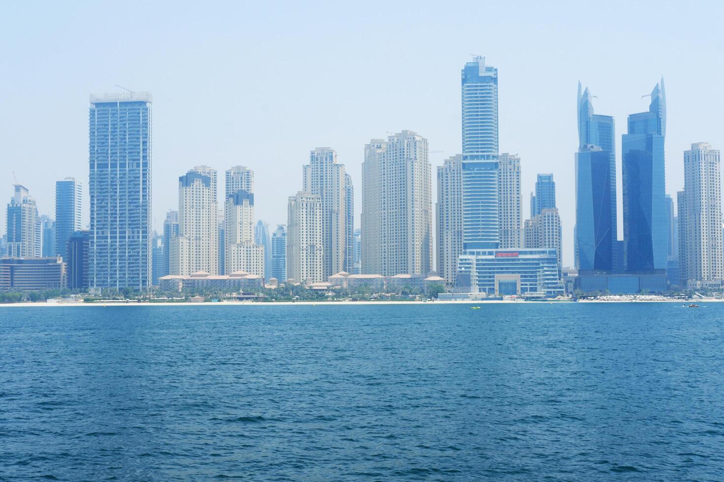 Dense high-rise buildings line the coast of Dubai under a hazy blue sky. Dubai, UAE - August 15, 2023 photo