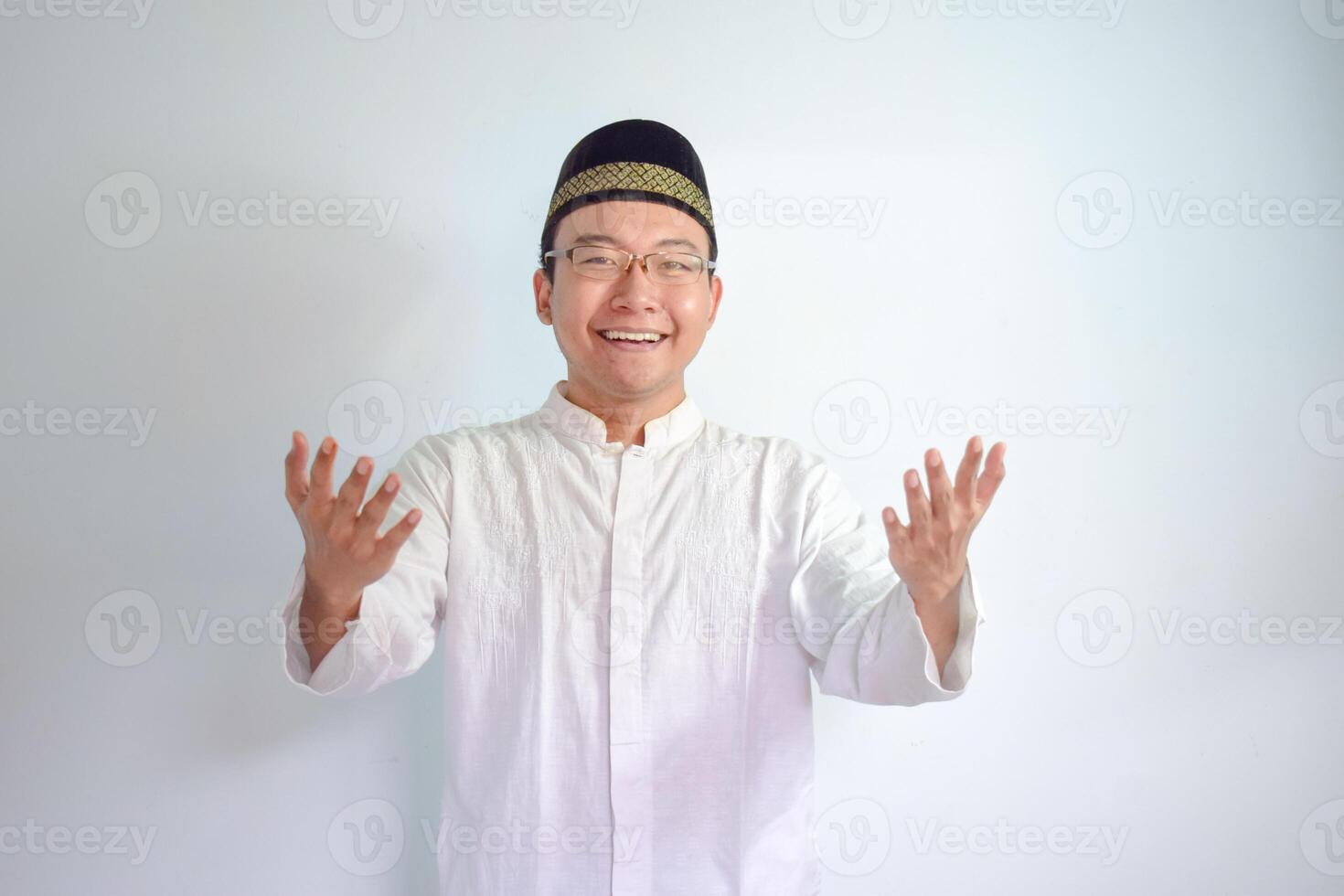 Asian Muslim man wearing glasses and white cloth smiling doing greeting pose for ramadhan and eid al fitr. Isolated white background photo