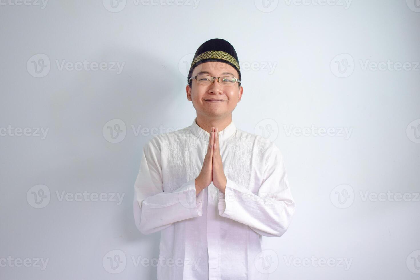 asiático musulmán hombre vistiendo lentes y blanco paño sonriente haciendo saludo actitud para ramadhan y eid Alabama fitr. aislado blanco antecedentes foto