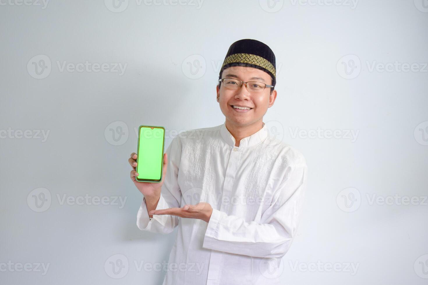 Asian Muslim man wearing glasses and white cloth pointing phone pose for ramadhan and eid al fitr. Isolated white background photo