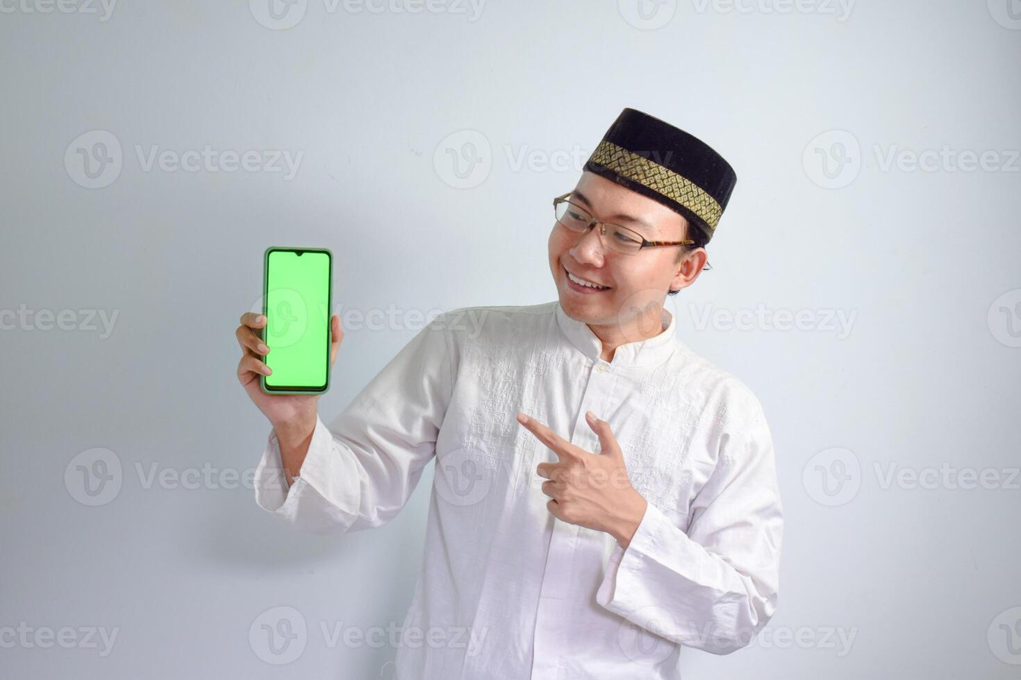 Asian Muslim man wearing glasses and white cloth pointing phone pose for ramadhan and eid al fitr. Isolated white background photo