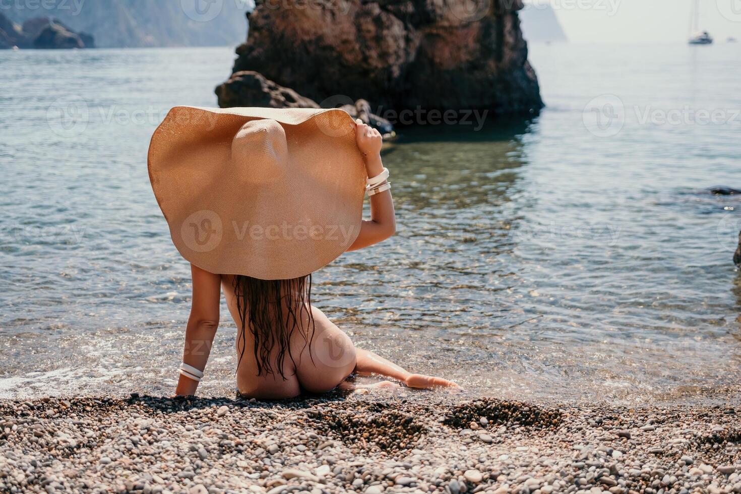 mujer viaje mar. contento turista en sombrero disfrutar tomando imagen al aire libre para recuerdos. mujer viajero posando en el playa a mar rodeado por volcánico montañas, compartiendo viaje aventuras viaje foto