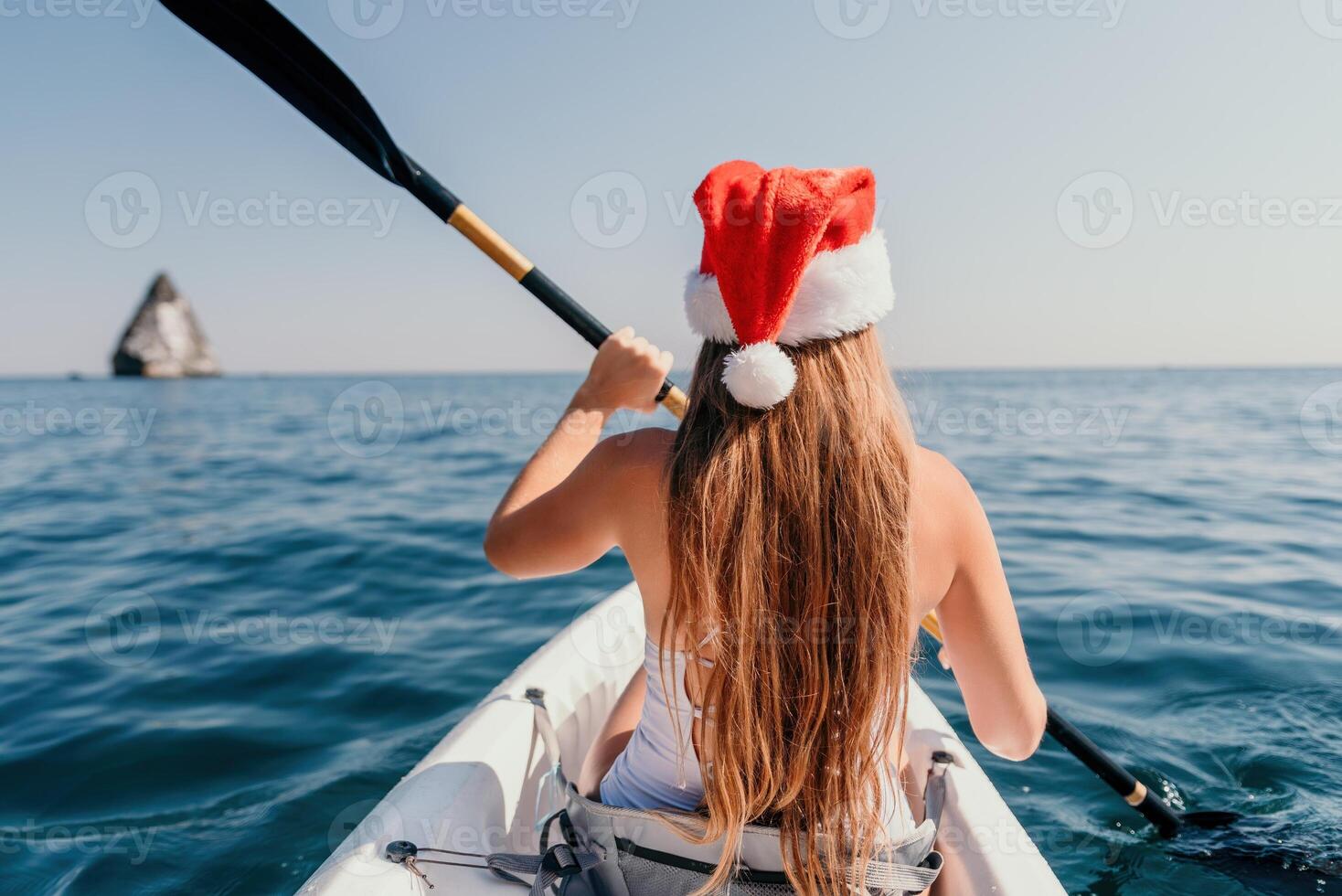 Woman in kayak back view. Happy young woman in Santa hat floating in kayak on calm sea. Summer holiday vacation and cheerful female people relaxing having fun on the boat. photo